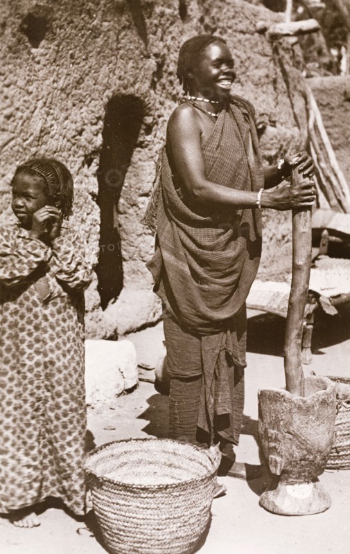 Grinding 'durra', Sudan. A Sudanese woman in traditional dress smiles as she uses a large pestle and mortar to grind 'durra', the grain of a cereal grass that is used to make bread. Omdurman, Sudan circa 1910. Omdurman, Khartoum, Sudan, Eastern Africa, Africa.