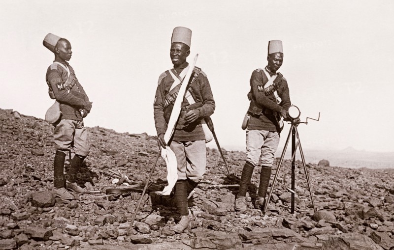 Sudanese signalmen in the Anglo-Egyptian army. Three Sudanese signalmen in the Anglo-Egyptian army operate a mirror signalling device on rocky ground. An original caption labels this image as: 'Battlefield, Omdurman', and suggests that it may have been taken around the time of the Battle of Omdurman (1898), which saw Mahdist Sudanese forces defeated by the British under the command of Lord Kitchener. Omdurman, Sudan, circa 1898. Omdurman, Khartoum, Sudan, Eastern Africa, Africa.