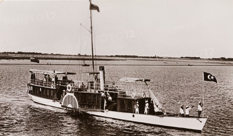 Paddle steamer on the River Nile. A paddle steamer named 'The Elfin' travels along the River Nile, flying a British Empire flag at its stern and a Ottoman Empire flag at its bow. Near Sudan, circa 1910. Sudan, Eastern Africa, Africa.