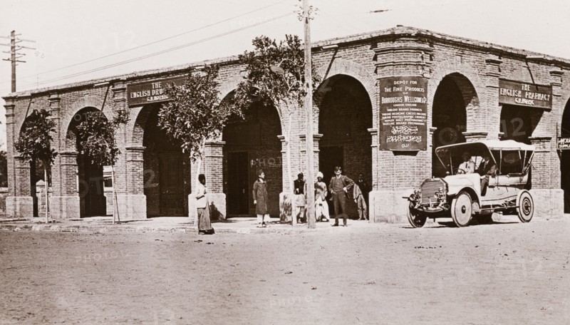 Outside the English Pharmacy, Khartoum. Exterior view of the English Pharmacy in Khartoum, an arcaded, brick building with a flat roof. Banners hanging from the building read 'The English Pharmacy' and 'The English Drugstore', along with an advertisement for 'Burroughs Wellcome & Co.' products. Khartoum, Sudan, circa 1910. Khartoum, Khartoum, Sudan, Eastern Africa, Africa.