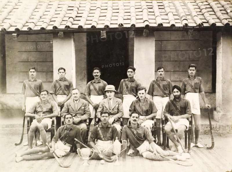 Portrait of an Indian police hockey team. Group portrait of an Indian police hockey team. Three British men pose at the centre of the group, surrounded by Indian players with their hockey sticks, who wear matching shirts and shorts. Two trophies and a hockey ball are positioned on the ground in front of them. India, circa 1940. India, Southern Asia, Asia.