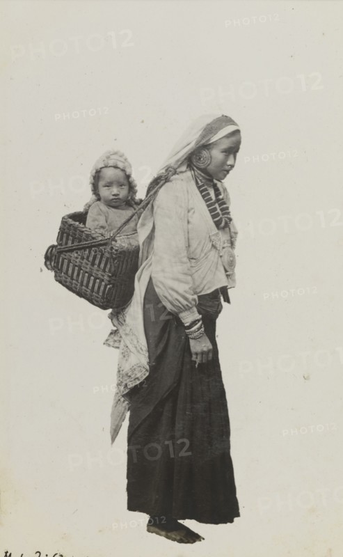 Portrait of a Nepalese woman and baby. Portrait of a Nepalese woman and baby. The women wears traditional dress including an ornate necklace, earrings and bracelets: her baby rides in a basket, securely strapped to her back and head. Nepal, circa 1922. Nepal, Southern Asia, Asia.