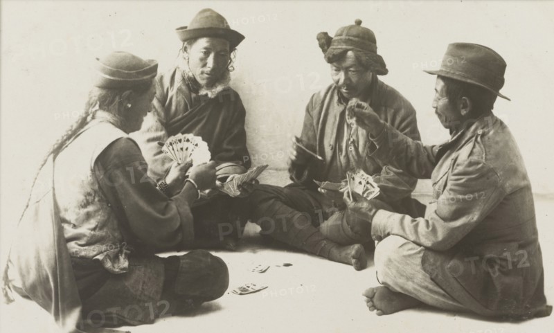 Rickshaw drivers enjoy a game of cards. Four rickshaw drivers sit cross-legged in a circle on the ground, each holding a hand of fanned-out playing cards during a game of cards. Probably Nepal, circa 1922. Nepal, Southern Asia, Asia.