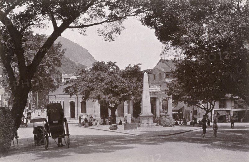 Market square in Wan Chai. A view of a market square at the foot of Morrison Hill in Wan Chai, where only a couple of street traders have set their stalls up by a tall, stone monument, which stands in the centre. Wan Chai, Hong Kong, China, circa 1903. Wan Chai, Hong Kong, China, People's Republic of, Eastern Asia, Asia.