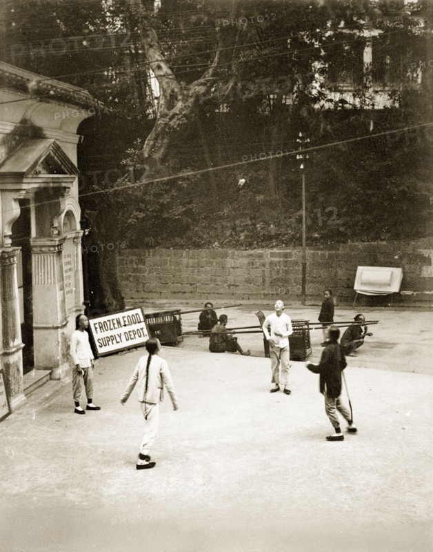 Playing football with a shuttlecock. Four young Chinese men play football with a shuttlecock outside the Dairy Farm office and frozen food depot. Their hair is worn in 'queues' (waist-long pigtails), in traditional Manchu style. Hong Kong, China, circa 1905. Hong Kong, Hong Kong, China, People's Republic of, Eastern Asia, Asia.