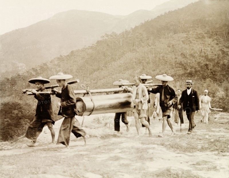 A working-class Chinese funeral procession. Four pallbearers carry the simply-constructed coffin of a working-class person to a rural burial site. A group of mourners follow behind, including one European man dressed in Western-style clothing. China, circa 1905. China, People's Republic of, Eastern Asia, Asia.
