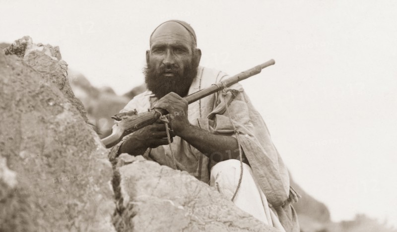 Portrait of an armed Afridi man. Portrait of an armed Afridi man, crouched behind a rock at Kohat Pass. Kohat, North West Frontier Province, India (Pakistan), circa 1925. Kohat, North West Frontier Province, Pakistan, Southern Asia, Asia.