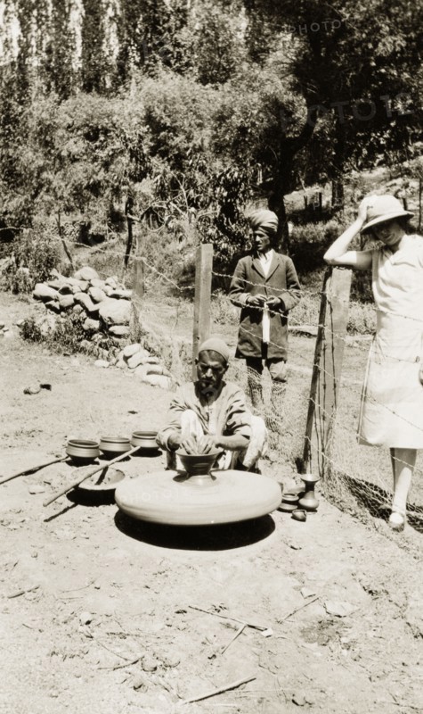 A potter in Srinagar. An Indian potter sits on the ground outdoors, shaping clay into a pot using a potter's wheel. Three completed pots are positioned in a row beside him. Srinagar, Jammu and Kashmir, India, circa 1927. Srinagar, Jammu and Kashmir, India, Southern Asia, Asia.