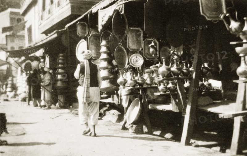 A copper bazaar. An Indian man in traditional dress walks past a row of market stalls crowded with goods at a copper bazaar. North West Frontier Province, India (Pakistan), circa 1927., North West Frontier Province, Pakistan, Southern Asia, Asia.