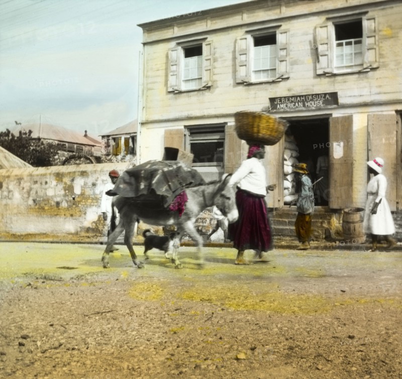 On the way to market', Antigua. A woman and donkey travel to market laden with goods, past an 'American House' in the centre of town. Probably St John's, Antigua, circa 1910. St John's, St John (Antigua and Barbuda), Antigua and Barbuda, Caribbean, North America .