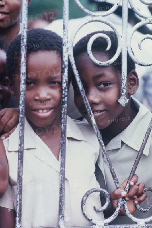 Two Jamaican schoolchildren. An official Jamaican Tourist Board photograph features two curious schoolchildren peering through iron railings at the Spanish Town Elementary School. Spanish Town, Jamaica, circa 1985. Spanish Town, St Catherine, Jamaica, Caribbean, North America .