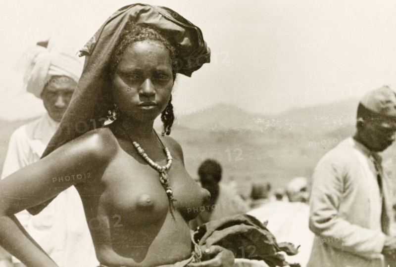 A young Eritean woman. Portrait of a young Eritean woman at a camel market. Naked from the waist up, she stands with one hand on her hip, wearing a headscarf and a beaded necklace. Eritrea, 1943. Eritrea, Eastern Africa, Africa.
