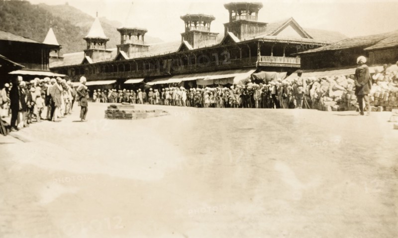 Crowds at a 'chowk' in Mandi, India. A crowd of people line up outside a row of shops with awnings at a 'chowk' (road junction) in Mandi. They appear to be waiting for some sort of parade as the street has been totally cleared. Mandi, Simla Hill States (Himachal Pradesh), India, 31 March 1920. Mandi, Himachal Pradesh, India, Southern Asia, Asia.