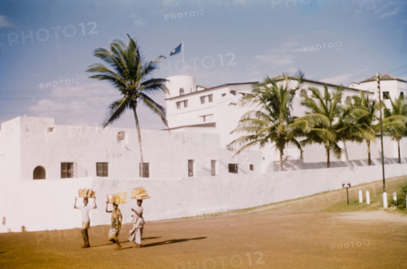 Breadsellers at Elmina Castle. Three breadsellers walk along a road adjacent to Elmina Castle. Elmina, Ghana, circa 1959. Elmina, Central (Ghana), Ghana, Western Africa, Africa.
