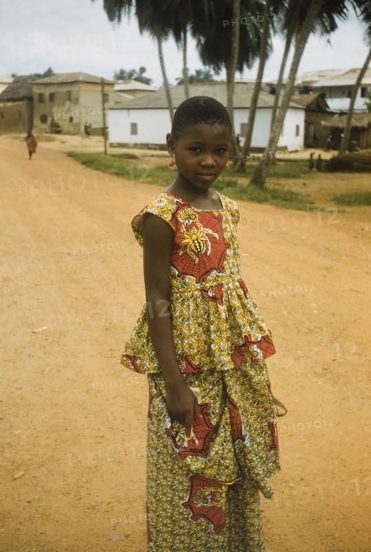 The red earrings'. Portrait of a Ghanaian girl standing on a road in Anomabu. She wears a two-piece cotton dress, decorated with a colourful print, and a pair of red earrings. Anomabu, Ghana, January 1958. Anomabu, Central (Ghana), Ghana, Western Africa, Africa.