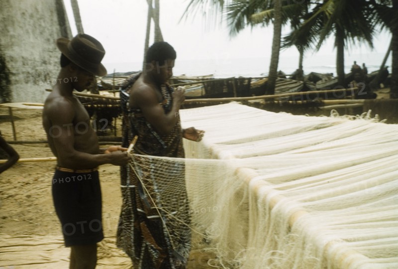 Mending the nets. Two men repair fishing nets at Anomabu beach. Anomabu, Ghana, January 1958. Anomabu, Central (Ghana), Ghana, Western Africa, Africa.