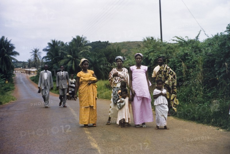 Churchgoers in Abandze. Families dressed in their Sunday best walk along a road to attend church in Abandze. Abandze, Ghana, circa 1958. Abandze, Central (Ghana), Ghana, Western Africa, Africa.