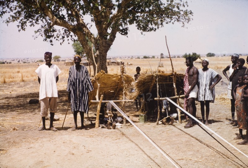 Boys weaving cloth at Pusiga, Ghana. Two young boys sit outdoors beneath thatched sun shelters as they weave strip cloth using heddle looms. Pusiga, Ghana, circa 1960. Pusiga, Upper East, Ghana, Western Africa, Africa.