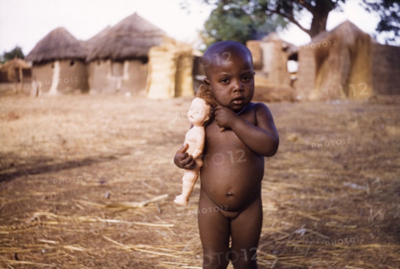 Ghanaian toddler with a European-style doll. Portrait of a naked young girl, aged about three, clutching a European-style doll. Near Bawku, Ghana, circa 1960. Bawku, Upper East, Ghana, Western Africa, Africa.