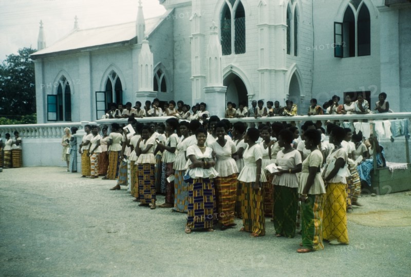 Students of a Wesleyan Girls' High School. Students of a Wesleyan Girls' High School gather outside a Methodist church at Cape Coast, dressed in a uniform of white blouses with skirts made from traditional kente cloth. Cape Coast, Ghana, 3 July 1960. Cape Coast, Central (Ghana), Ghana, Western Africa, Africa.