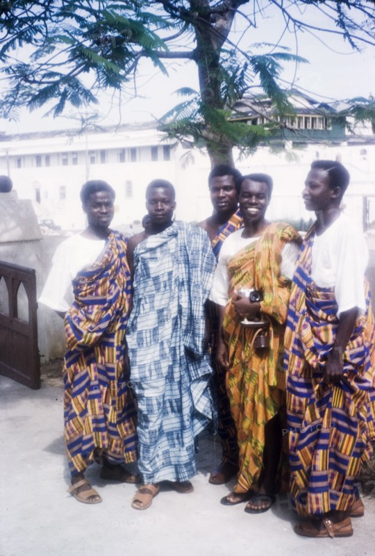 Men in traditional Ghanaian dress. A group of Ghanaian men pose for a portrait wearing traditional dress. An original caption identifies them as 'service and office staff', possibly employees of the Ministry of Education. Ghana, 23 April 1960. Ghana, Western Africa, Africa.