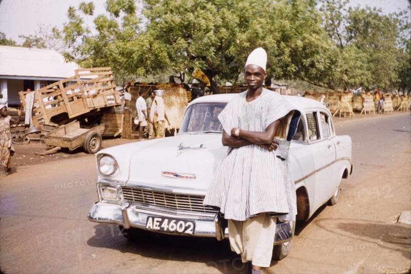 Mumuni Bawumia, Paramount Chief of Kperiga. Mumuni Bawumia (c.1927-2002), Paramount Chief of Kperiga, poses by his car on a street in Tamale. Tamale, Ghana, circa 1961. Tamale, North (Ghana), Ghana, Western Africa, Africa.