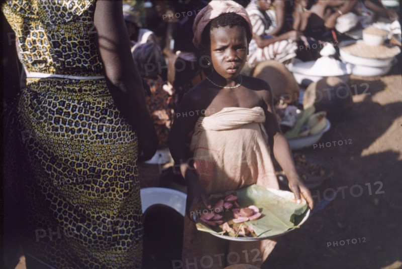 Kola nut seller. A young girl sells kola nuts from a leaf-lined plate at Tamale market. Tamale, Ghana, circa 1961. Tamale, North (Ghana), Ghana, Western Africa, Africa.