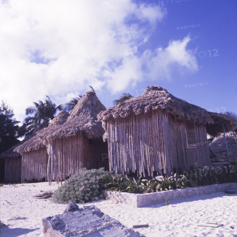 Beach huts at San Pedro, Belize. Four square, bamboo beach huts with thatched roofs stand in a row on the beachfront at San Pedro. Ambergris Caye, Belize, circa 1975. San Pedro, Ambergris Caye, Belize, Central America, North America .
