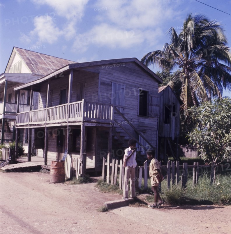 Wooden house in Belize. Two boys chat on a street corner outside a wooden, two-storey house in Danriga, which features a veranda and balcony. Danriga, Belize, circa 1975. Dangriga, Stann Creek, Belize, Central America, North America .