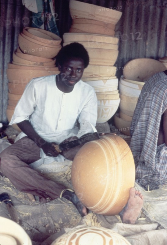 A Hausa potter decorates a bowl. A Hausa potter uses a metal tool to inscribe patterns onto a clay bowl. Kano, Nigeria, circa 1975. Nigeria, Western Africa, Africa.