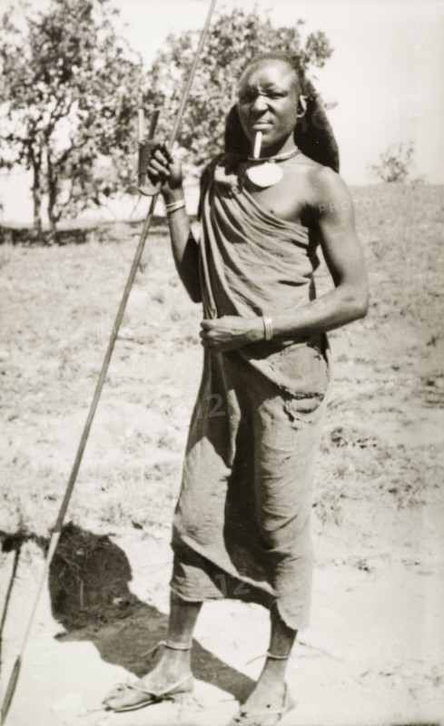 Kenyan man in traditional dress. Full-length portrait of a Kenyan man in traditional dress, adorned with jewellery and posing with a spear. Rift Valley, Kenya, circa 1933., Rift Valley, Kenya, Eastern Africa, Africa.