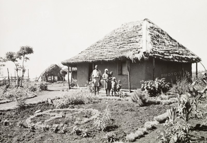 A Kikuyu family outside their home. A Kikuyu family pose in the garden outside their new, Western-style house. South Nyeri, Kenya, 1936. Nyeri, Central (Kenya), Kenya, Eastern Africa, Africa.
