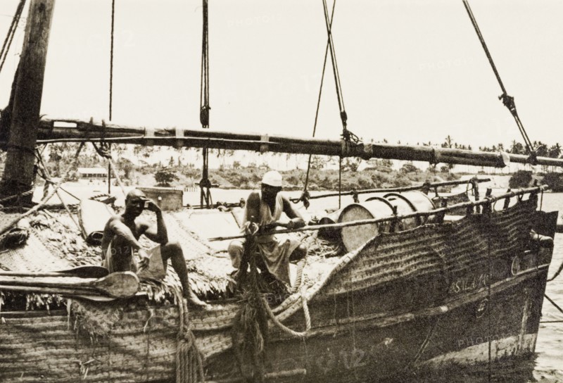 Dhow in Old Mombasa harbour. Two men perch on the edge of a dhow moored in Old Mombasa harbour. Mombasa, Kenya, 1933. Mombasa, Coast, Kenya, Eastern Africa, Africa.