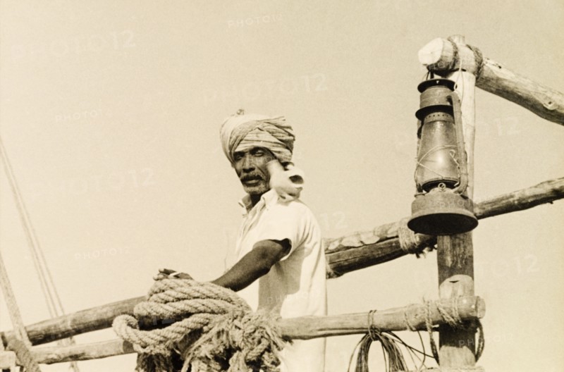 Sailor with a seabird. A turbaned dhow captain stands on the deck of his boat with a seabird resting on his shoulder. Malindi, Kenya, 1947. Malindi, Coast, Kenya, Eastern Africa, Africa.