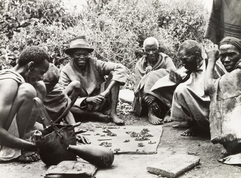 Telling fortunes by beans'. A group of Kikuyu men gather around to read their fortunes by scattering beans on the ground. South Nyeri, Kenya, 1936. Nyeri, Central (Kenya), Kenya, Eastern Africa, Africa.