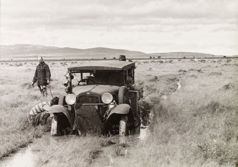 Stuck in the mud. Several men attend to a car, which is stuck in the mud on a flooded country track. North Tanganyika Territory (Tanzania), circa 1933. Tanzania, Eastern Africa, Africa.