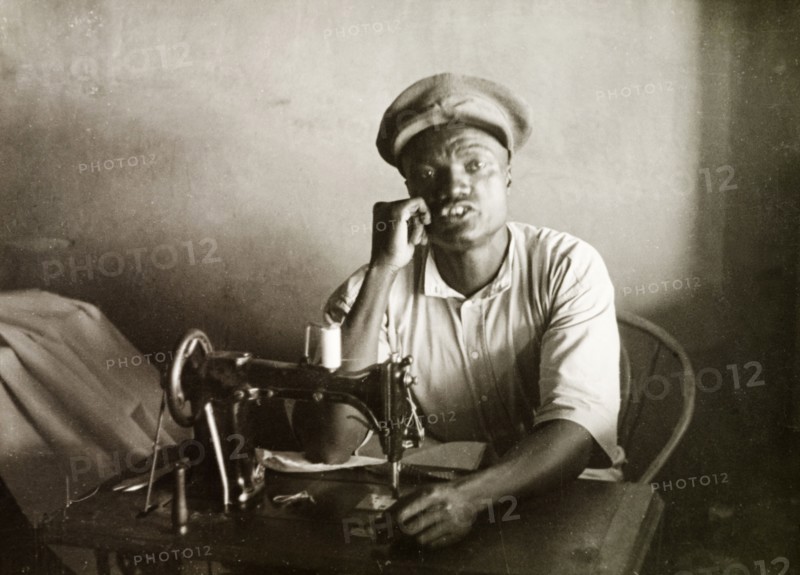 A Swahili tailor. A Swahili tailor sits behind a sewing machine at his work desk in Mombasa. Mombasa, Kenya, 1947. Mombasa, Coast, Kenya, Eastern Africa, Africa.