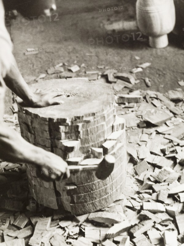 Shaping the shell of an atumpan drum. A craftsman uses a mallet on a section of timber, knocking out small blocks of wood to shape the shell of an atumpan drum. Ghana, circa 1965. Ghana, Western Africa, Africa.
