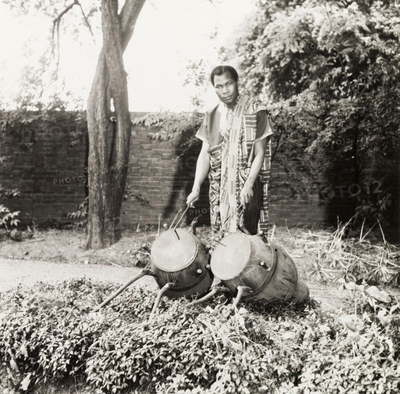 Asante man with atumpan drums. An Asante (Ashanti) man poses with a pair of ceremonial atumpan talking drums, ready to play with a hooked drumstick in each hand. Ghana, circa 1965. Ghana, Western Africa, Africa.