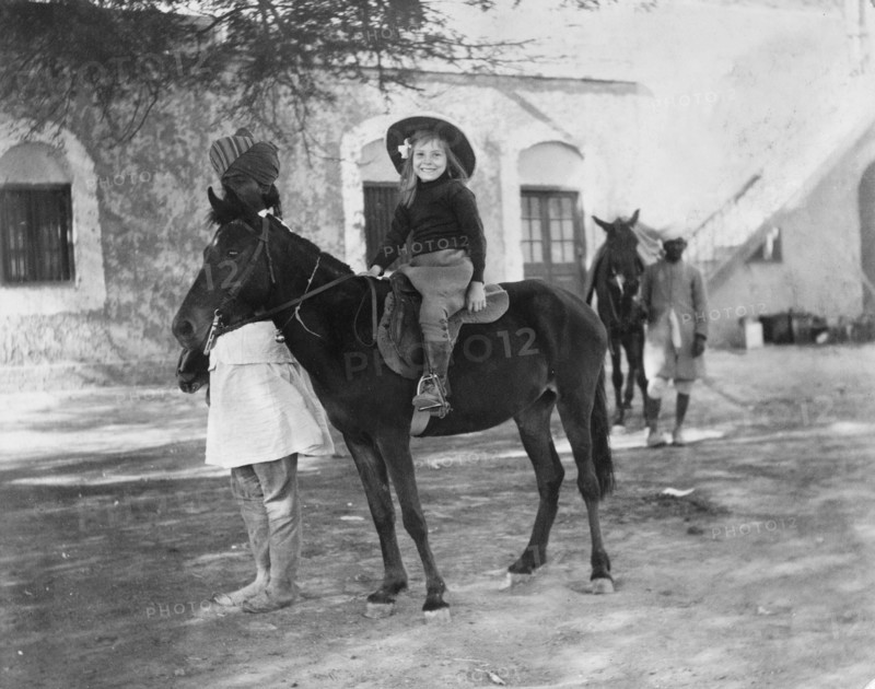 Riding a pony led by a 'sowar'. Margaret Lawrence (b.1904), the daughter of Phyllis and Sir Henry Staveley Lawrence (Collector of Karachi), rides a pony led by a turbaned 'sowar' (cavalry soldier) of the Indian Army. Karachi, India (Pakistan), circa 1912. Karachi, Sindh, Pakistan, Southern Asia, Asia.