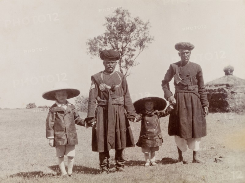 The Lawrence boys with Indian attendants. George (b.1899) and Henry (b.1902), the sons of Phyllis and Sir Henry Staveley Lawrence (a British civil servant), hold hands with two traditionally dressed Indian attendants. India, circa 1905. India, Southern Asia, Asia.