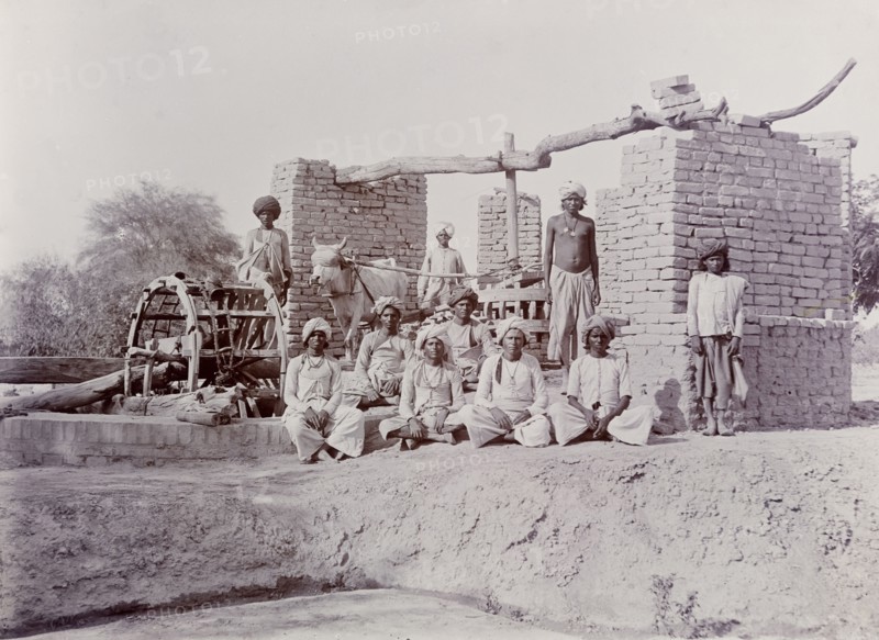 A bullock-driven water wheel, India. A group of Indian labourers pose for an outdoor portrait beside a bullock-driven water wheel. India, circa 1925. India, Southern Asia, Asia.