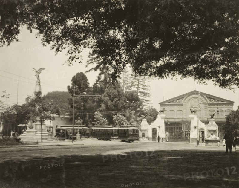 A street tram in Lima. A tram travels around the corner of a street in Lima, past a grand, colonial-style building and a stone monument topped with the statue of a winged figure. Lima, Peru, circa 1920. Lima, Lima Metropolitana, Peru, South America, South America .