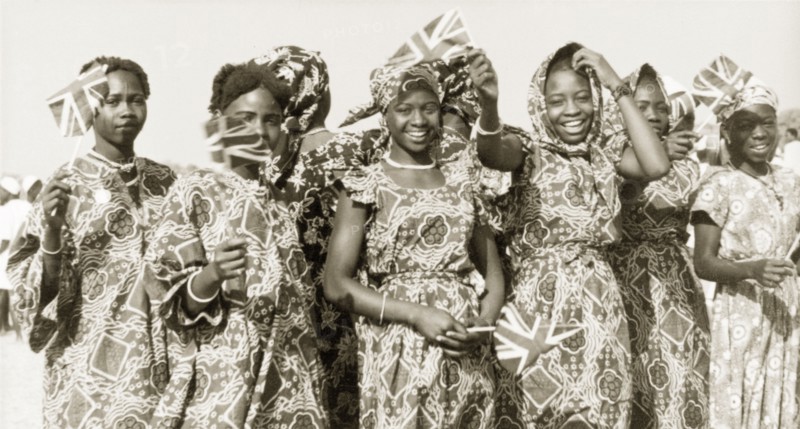 Flags for Queen Elizabeth II, Kaduna. Young women in traditional Nigerian dress wave union jack flags to welcome Queen Elizabeth II and the Duke of Edinburgh on their royal visit to Kaduna Children's Village. Kaduna, Nigeria, February 1956. Kaduna, Kaduna, Nigeria, Western Africa, Africa.