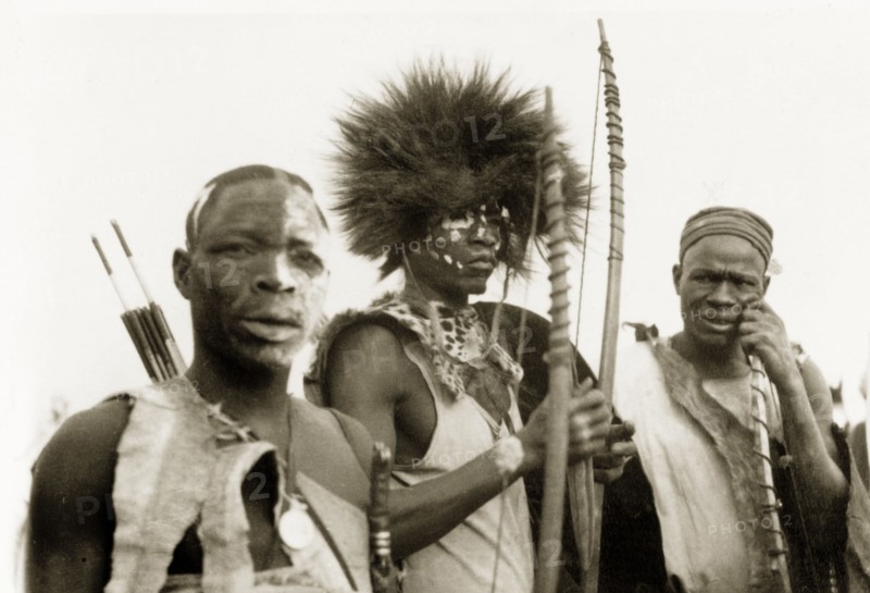 Nigerian hunters with bows and arrows. Portrait of three Nigerian hunters holding bows and arrows. They wear clothing made from animal skin and have their faces decorated with face paint. Nigeria, circa 1955. Nigeria, Western Africa, Africa.