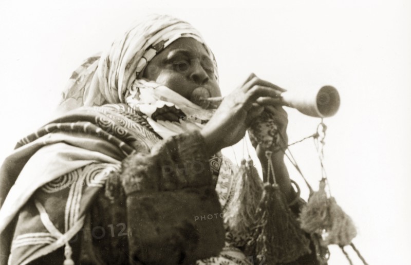 A Nigerian musician. A Nigerian musician plays a trumpet decorated with tassels. Nigeria, circa 1955. Nigeria, Western Africa, Africa.