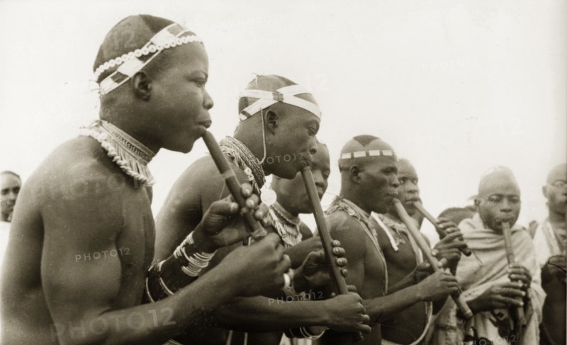 Nigerian pipe players. A group of Nigerian musicians gather to play pipes. Naked from the waist up, they wear decorative headbands around their shaven heads and are adorned with beaded necklaces and armbands. Nigeria, circa 1955. Nigeria, Western Africa, Africa.