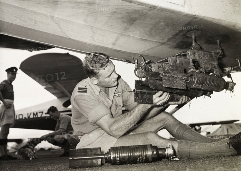 Kenya Police Airwing officer attaches missiles. Ian Cuthbert, an officer of the Kenya Police Airwing, attaches a small missile to the underside of an aircraft. Kenya, circa 1955. Kenya, Eastern Africa, Africa.