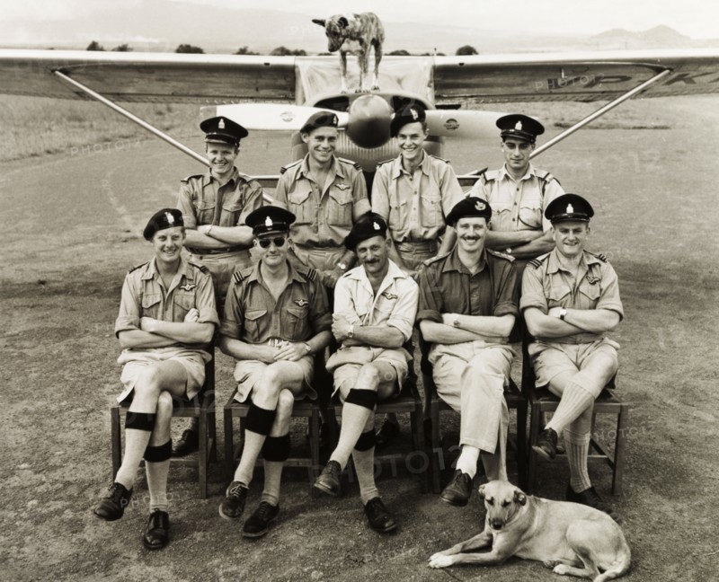 Kenya Police Airwing officers. Nine uniformed officers of the Kenya Police Airwing assemble for a group portrait with their dogs in front of a light aircraft at Mweiga operations base. Mweiga, Nyeri, Kenya, circa 1955. Nyeri, Central (Kenya), Kenya, Eastern Africa, Africa.