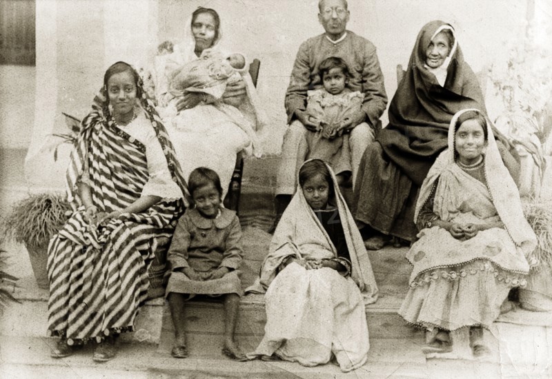 Portrait of an Indian family. Group portrait of an Indian family wearing traditional dress. Four sisters sit at the front with their parents and grandmother behind them holding a toddler and a baby. India, circa 1920. India, Southern Asia, Asia.